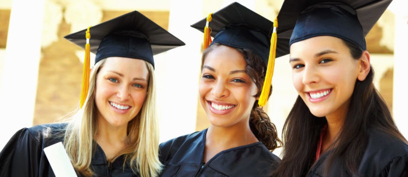 Three female graduates stand together wearing caps and gowns while holding their diplomas 